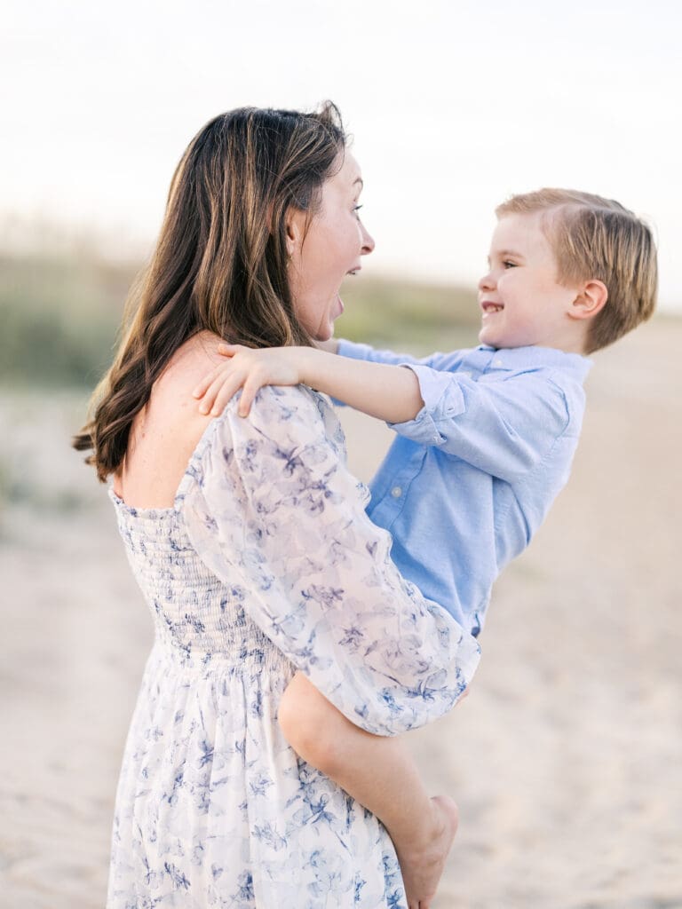 Mom smiling and holding toddler boy at the beach 