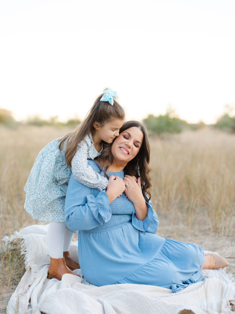 Mom dressed in blue cuddling with daughter at Pleasure House Point field 