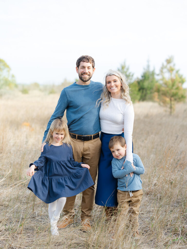 Family of four dressed in blue in field by Norfolk family photographer Ashley Brickner 