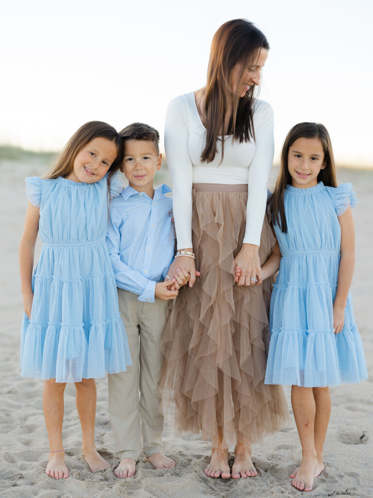 Mom holding hands with three kids in blue standing on beach by Norfolk family photographer Ashley Brickner 