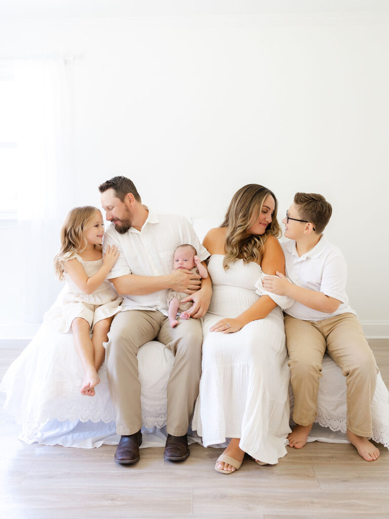 Family of five dressed in neutrals sitting on bed for Hampton Roads newborn photography session by Ashley Brickner 