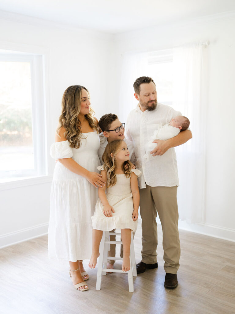Family of five in neutral clothing in studio looking at newborn baby boy 