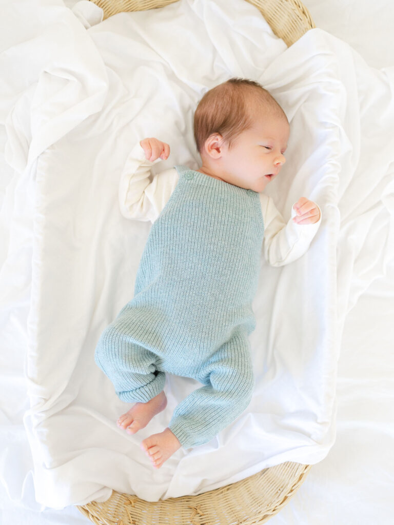 Newborn Baby boy in blue knit outfit laying in basket with white sheets