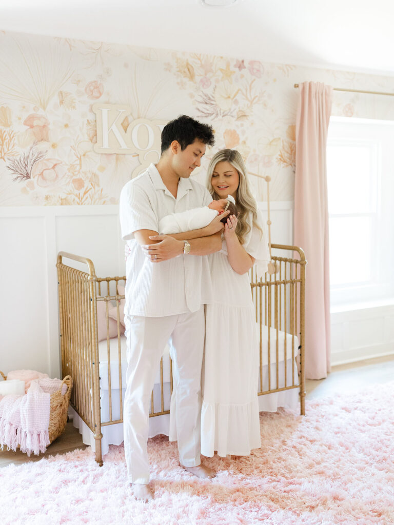 Mom and dad holding swaddled baby girl in a floral nursery during their Virginia Beach newborn session