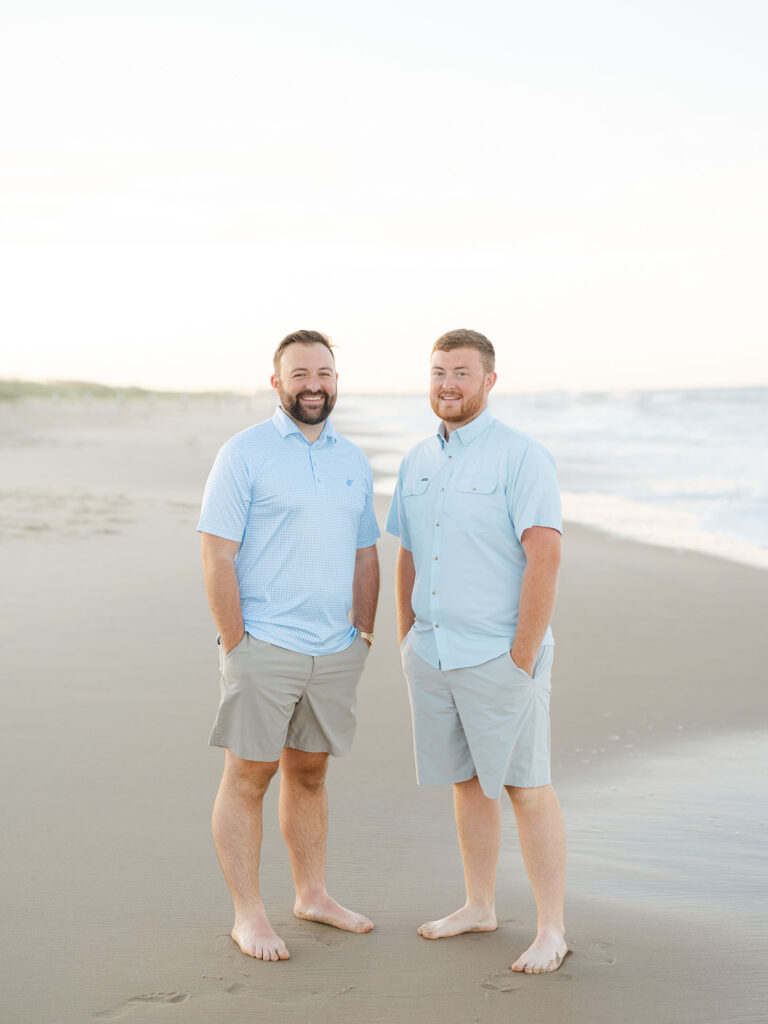 Two men dressed in blue and white standing on Sandbridge beach posing for photos 