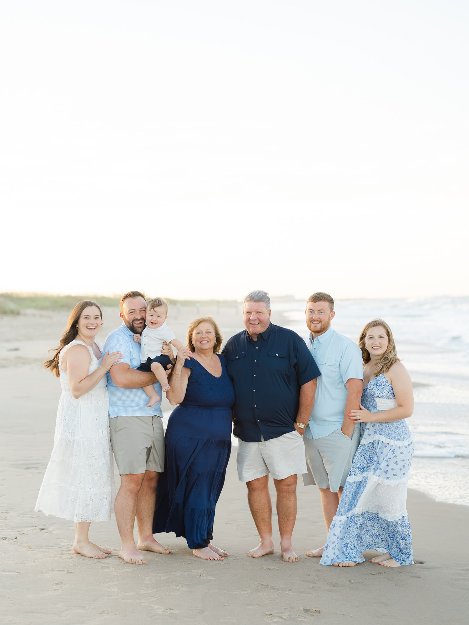 Extended family dressed in blue standing on beach by Sandbridge beach family photographer Ashley Brickner