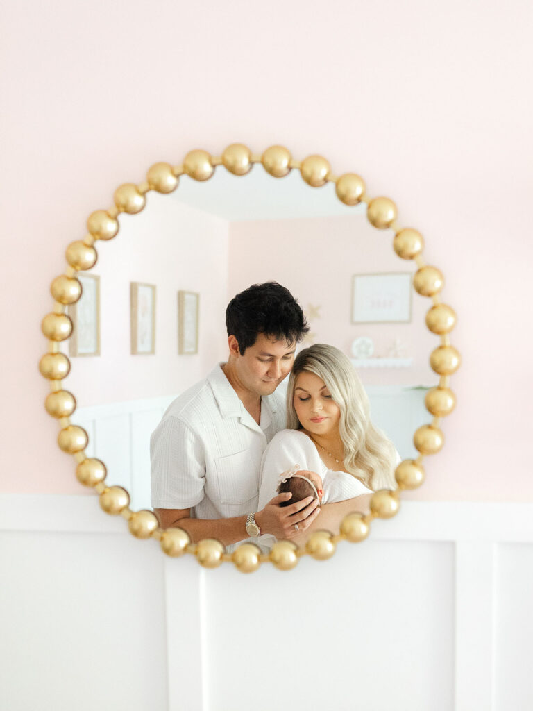 Reflection in gold mirror of a couple holding newborn baby girl by Chesapeake Newborn Photographer Ashley Brickner