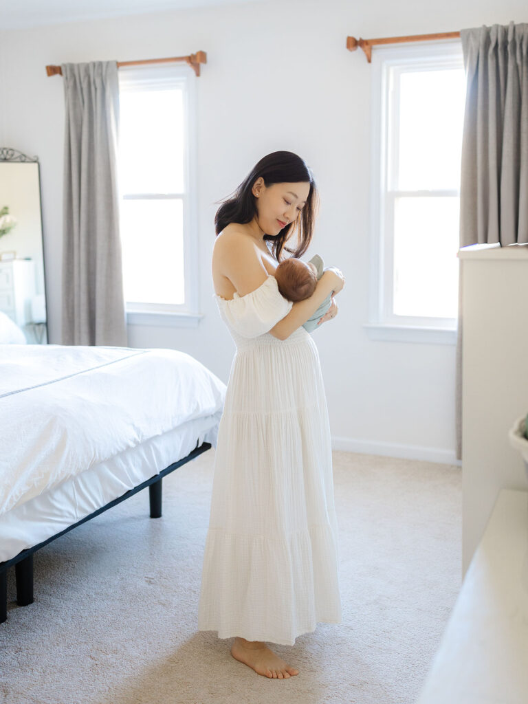 Mom in white dress holding newborn baby boy for a lifestyle newborn session