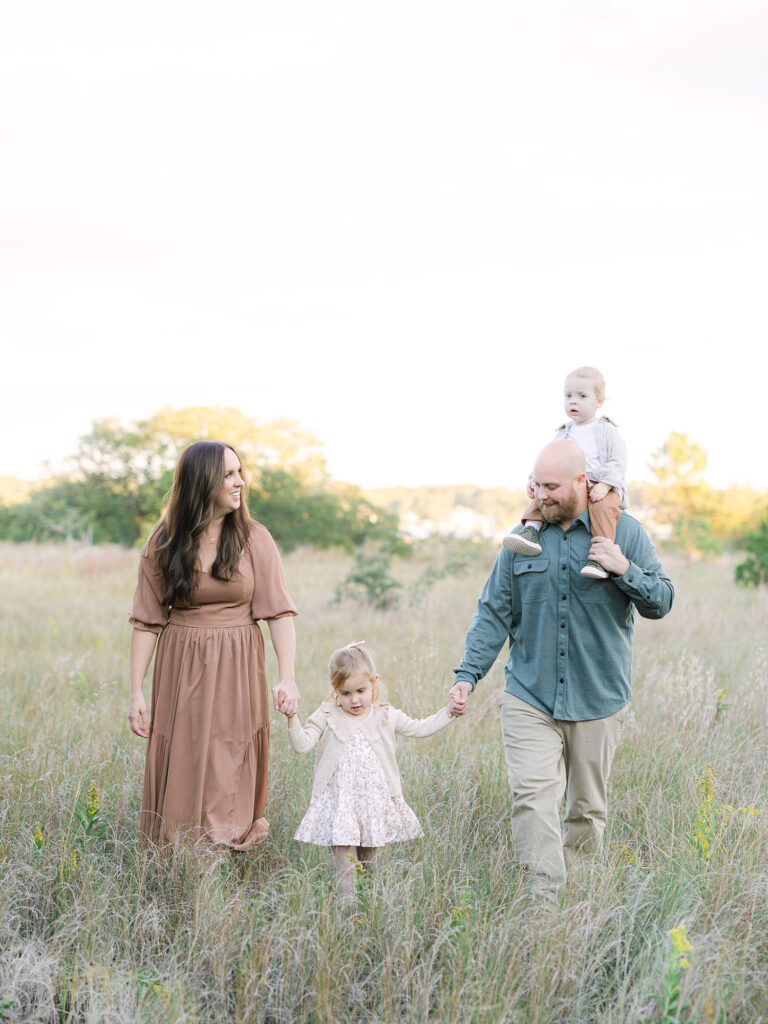 Family of four in neutral clothing walking in field at Pleasure House Point 