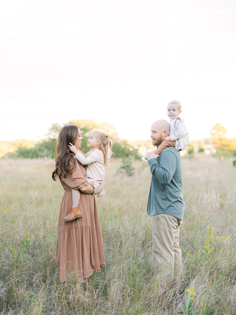 Family of four in neutral and green clothes standing in field by Hampton Roads Family Photographer Ashley Brickner 