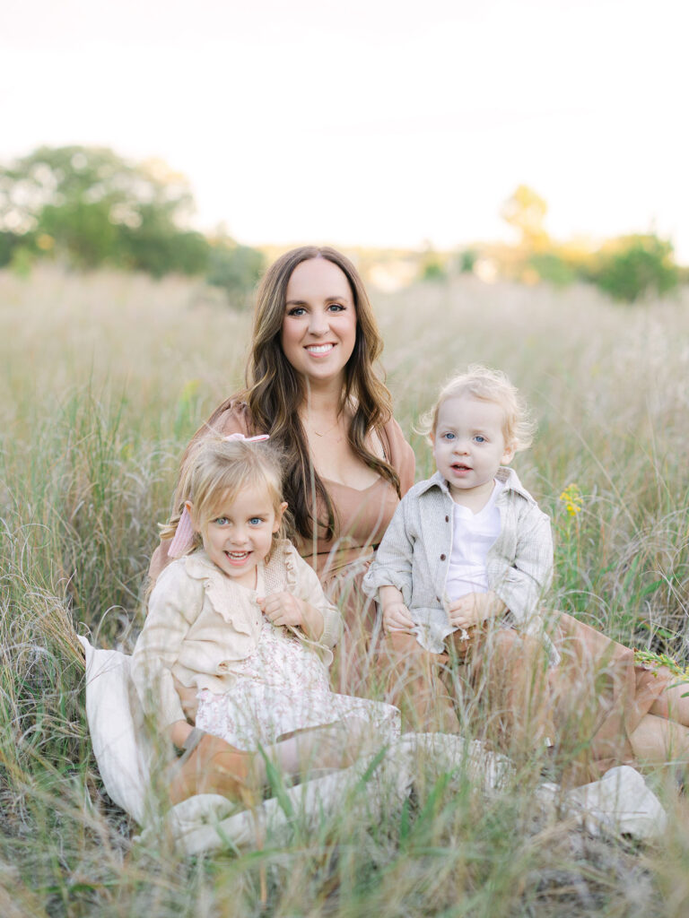 Mother and toddler daughter and son sitting in field at Pleasure House Point 