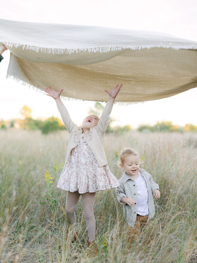 Toddler girl and toddler boy jumping under neutral blanket by Hampton Roads Family Photographer Ashley Brickner 