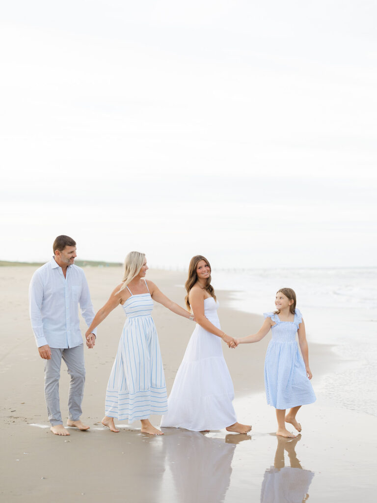Family of four holding hands and walking on the beach by Virginia Beach family portraits photographer Ashley Brickner