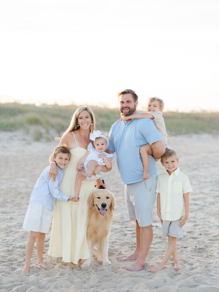 Family of six dressed in blue and yellow standing on North end beach with their yellow lab