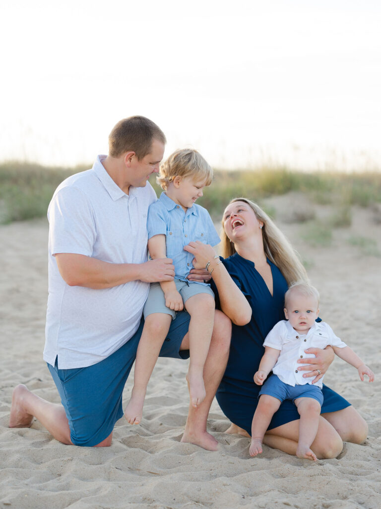 Family of four dressed in blue and white kneeling on the beach by Virginia Beach family portraits photographer Ashley Brickner