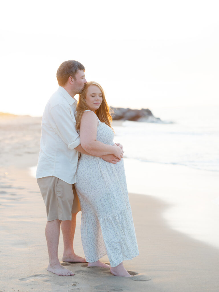 Husband holding pregnant wife's belly standing on beach 