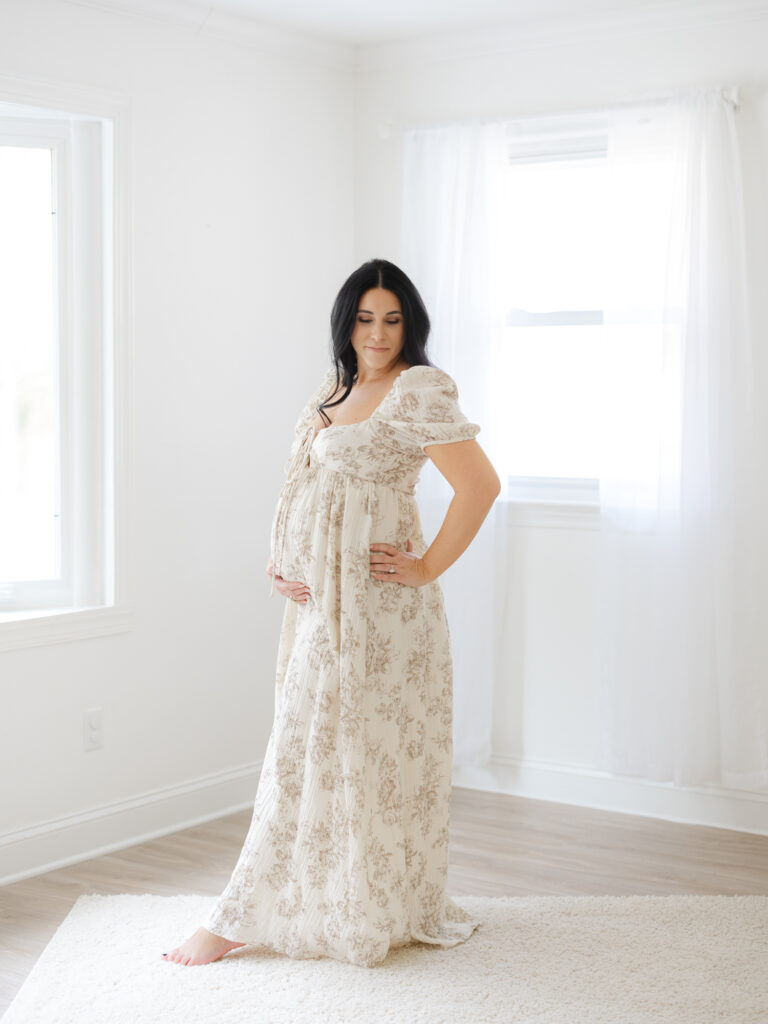 Pregnant mama holding her belly wearing floral maxi dress in studio by Virginia Beach maternity portraits photographer Ashley Brickner 