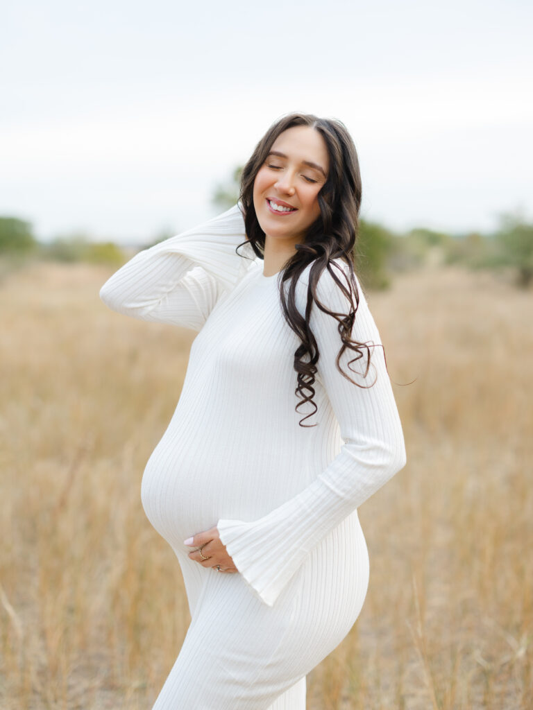 Pregnant mom wearing white dress standing in field by Virginia Beach maternity portraits photographer Ashley Brickner 