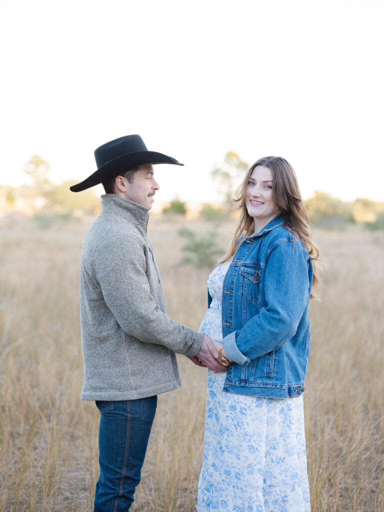 Husband holding pregnant wife's belly standing in field by Virginia Beach maternity portraits photographer Ashley Brickner 