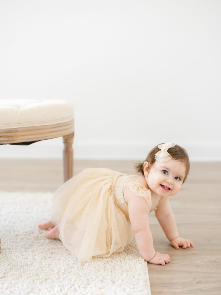 Toddler girl in neutral dress crawling in studio by photographer who specializes in Hampton Roads cake smash photography