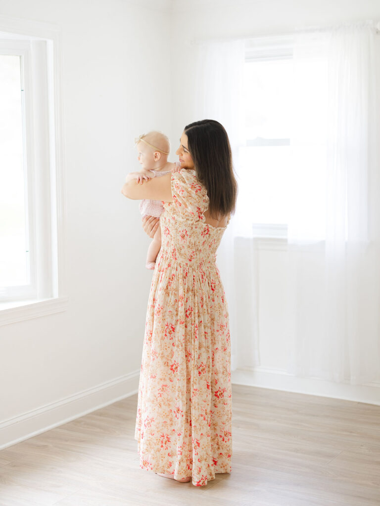 Mom in floral maxi dress holding girl by photographer who specializes in Hampton Roads cake smash photography