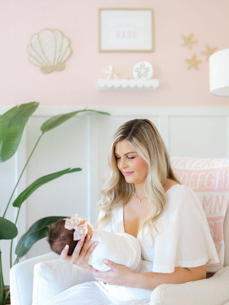 Mom in white dress holding swaddled newborn baby girl in nursery 