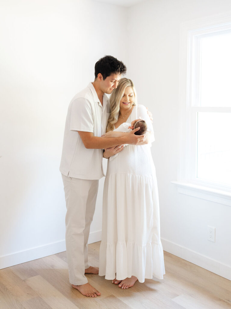 Mom and dad dressed in white holding newborn baby girl 