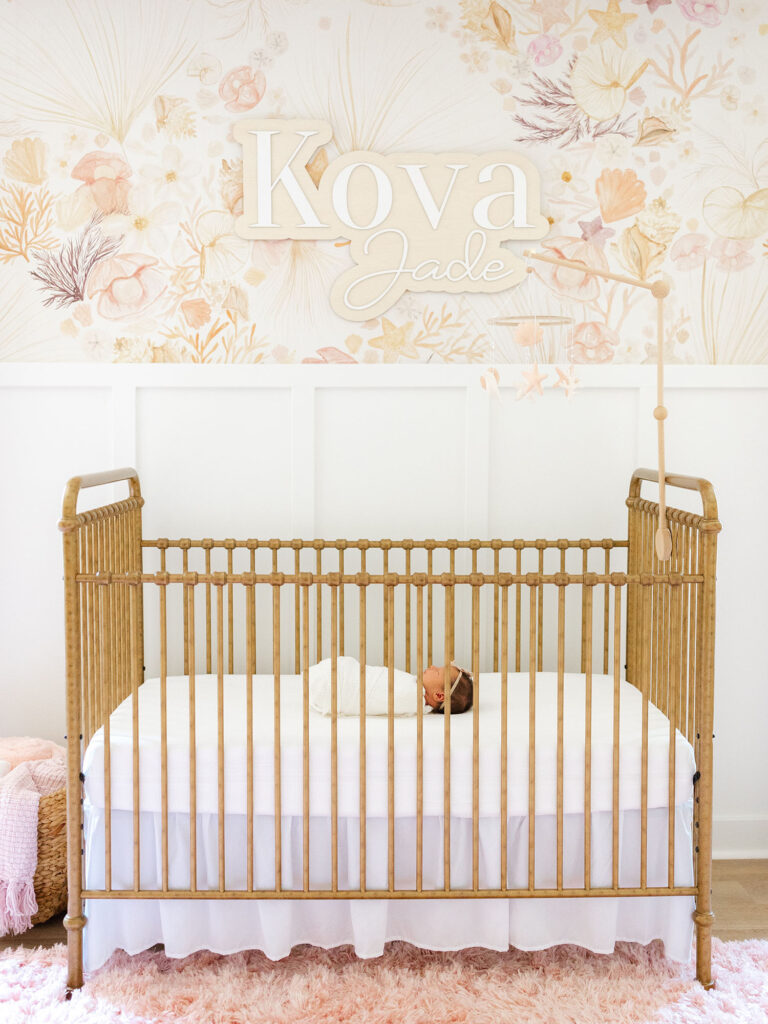 Newborn swaddled baby girl laying in brass crib in floral and pink nursery 