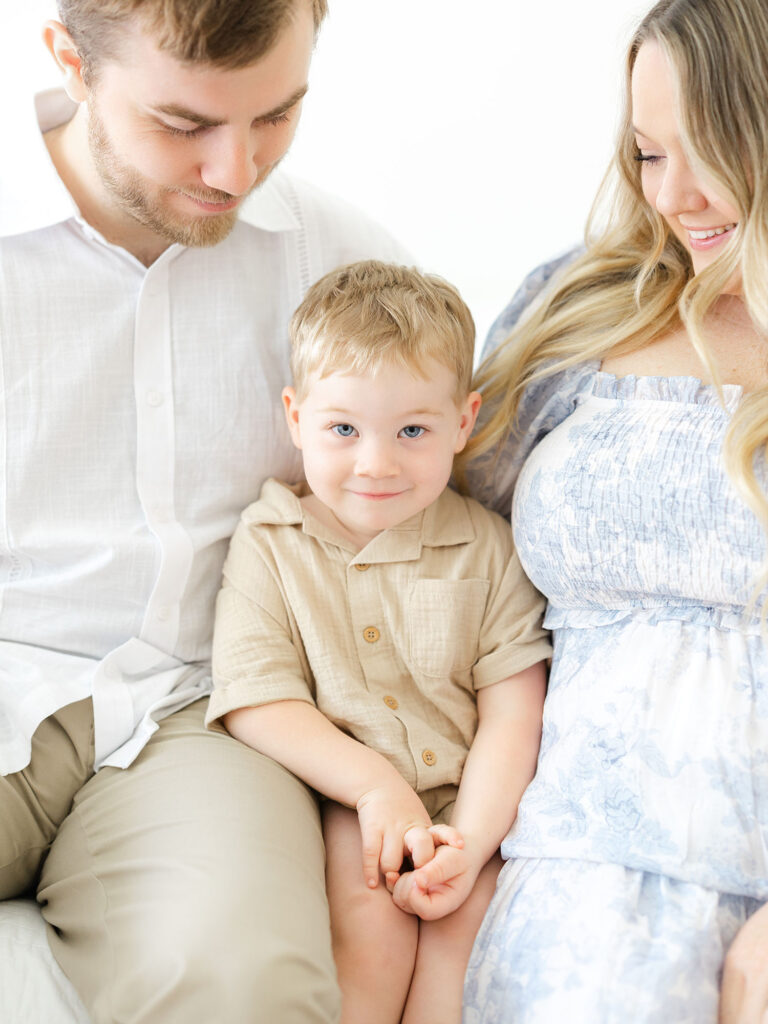 Mom and dad with toddler boy sitting on their lap in studio during Virginia Beach mini session by Ashley Brickner 