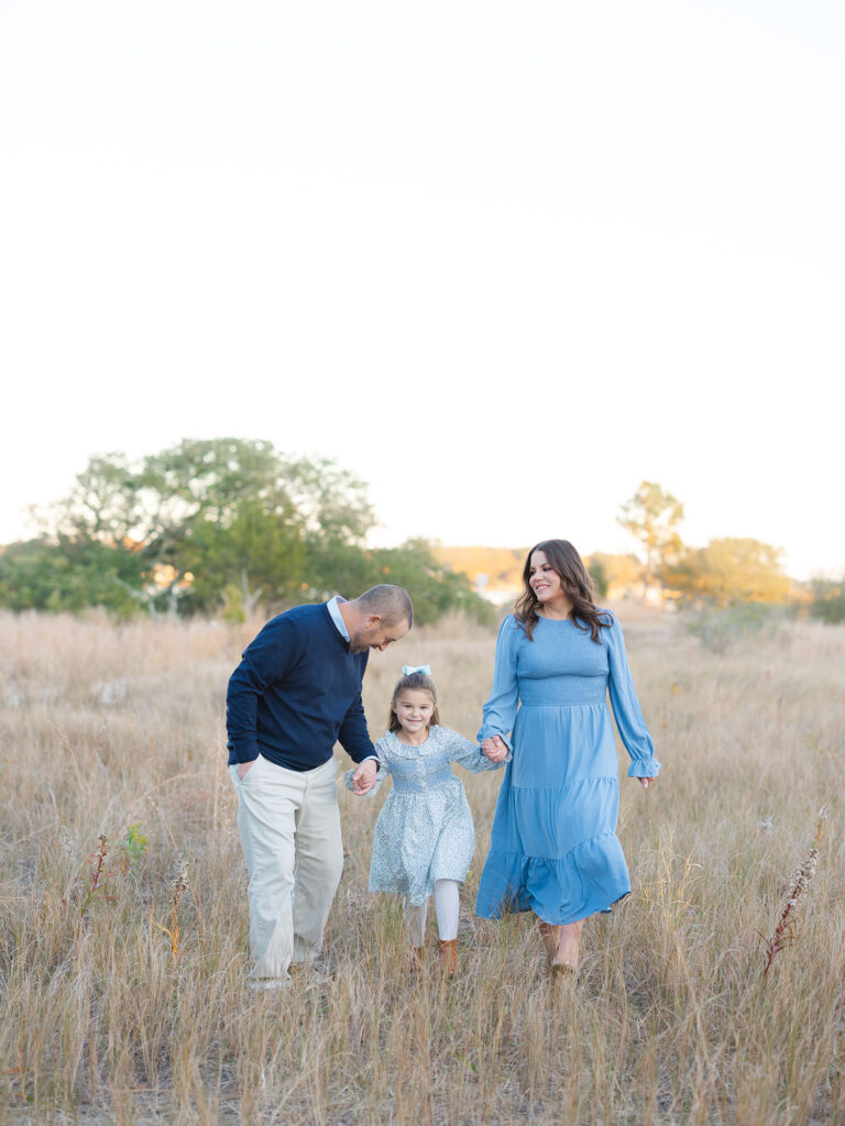 Family of three wearing blue walking in a field holding hands by Virginia family photographer Ashley Brickner 