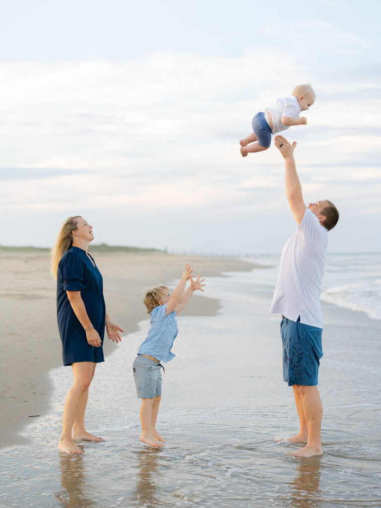 Family of four at north end beach watching little brother be thrown into the air dressed in blue and white 