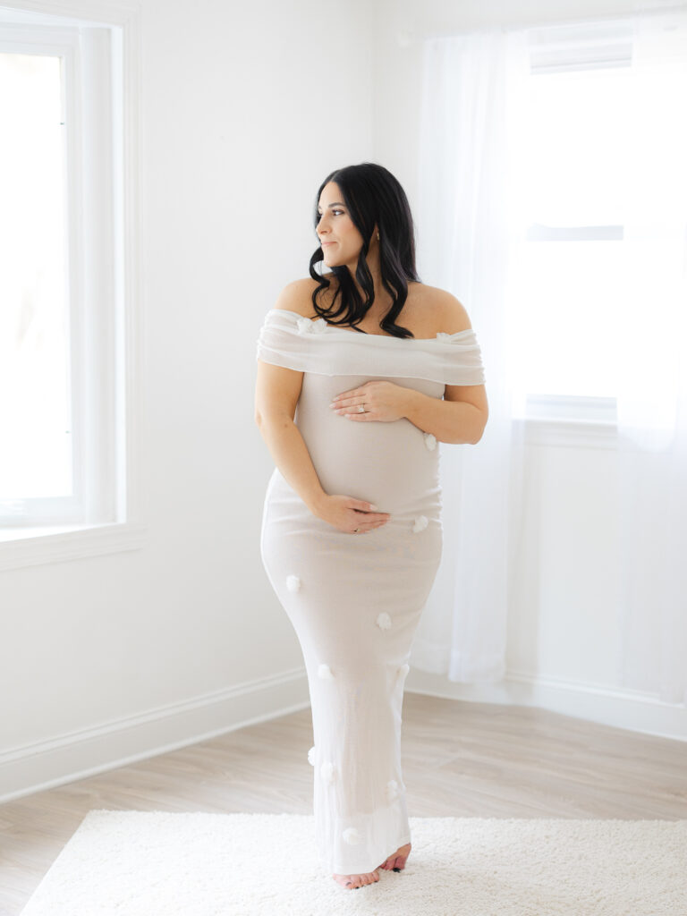 Pregnant mom standing in studio holding belly and looking through window by Virginia Maternity Photographer Ashley Brickner 