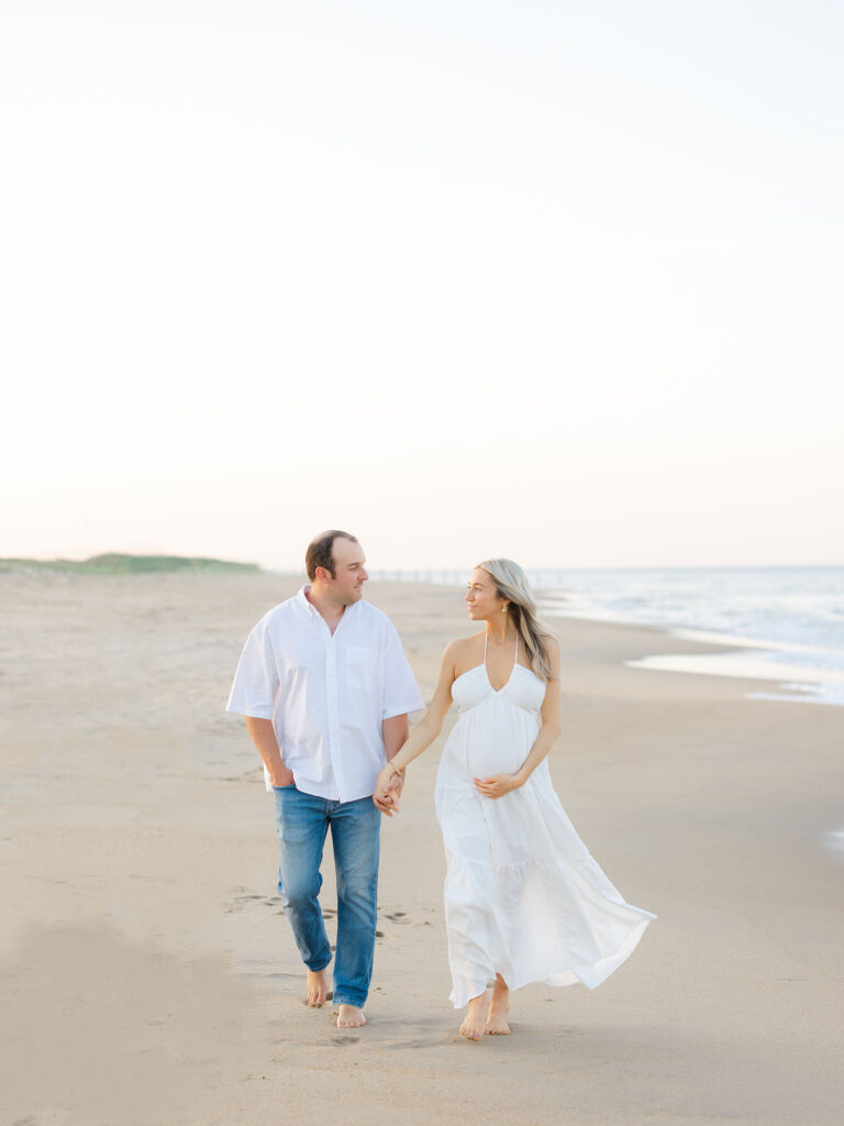 Pregnant mom and dad walking on beach at the north end in Virginia Beach 