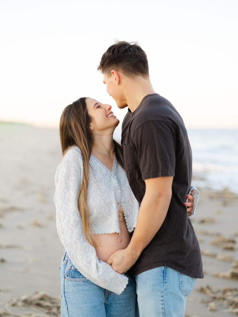 Husband and wife standing on beach and laughing by Virginia Maternity Photographer Ashley Brickner 