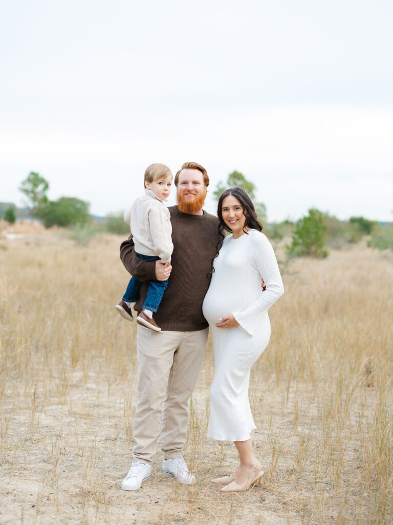 Pregnant mom, dad, and toddler boy standing and posing in field by Virginia Maternity Photographer Ashley Brickner 