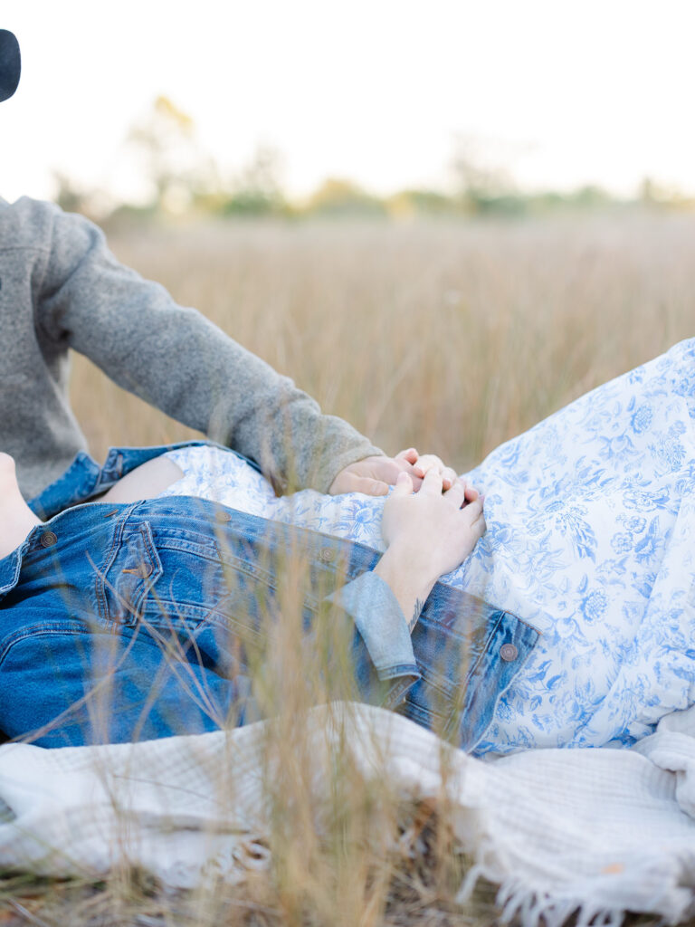 Mom and dad holding belly in field at Pleasure House Point 