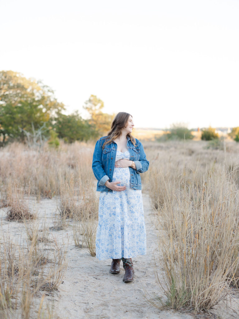 Pregnant mom in blue floral dress standing in field holding belly by Virginia Maternity Photographer Ashley Brickner 