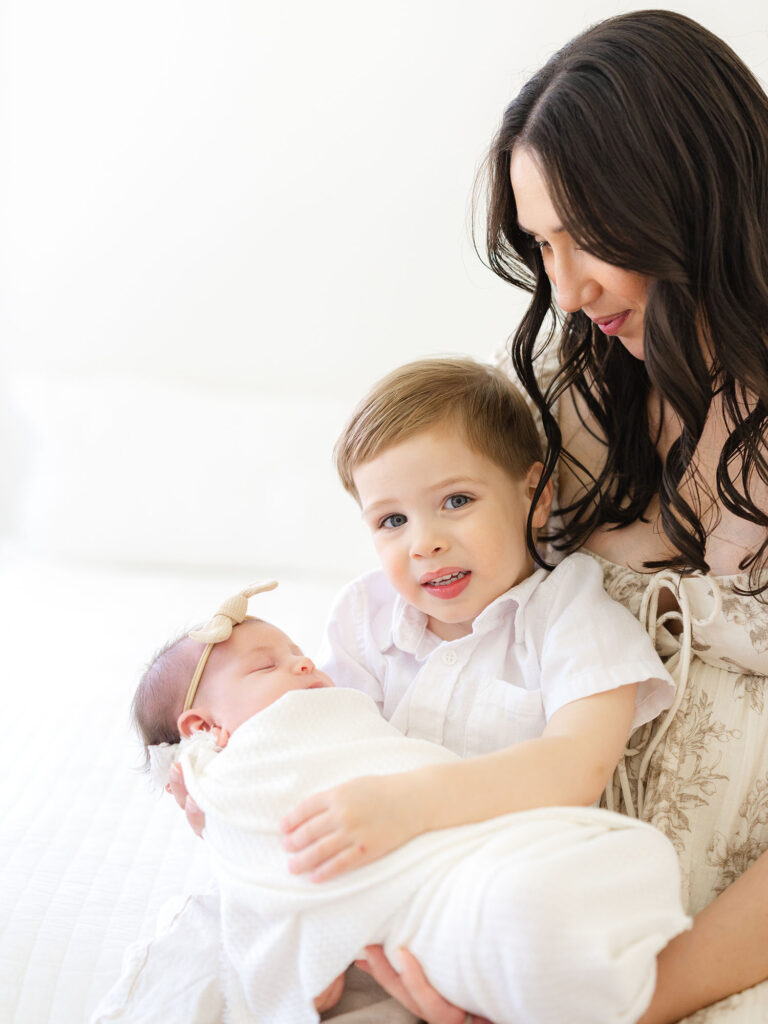 Mom holding toddler boy and swaddled newborn baby girl in studio 