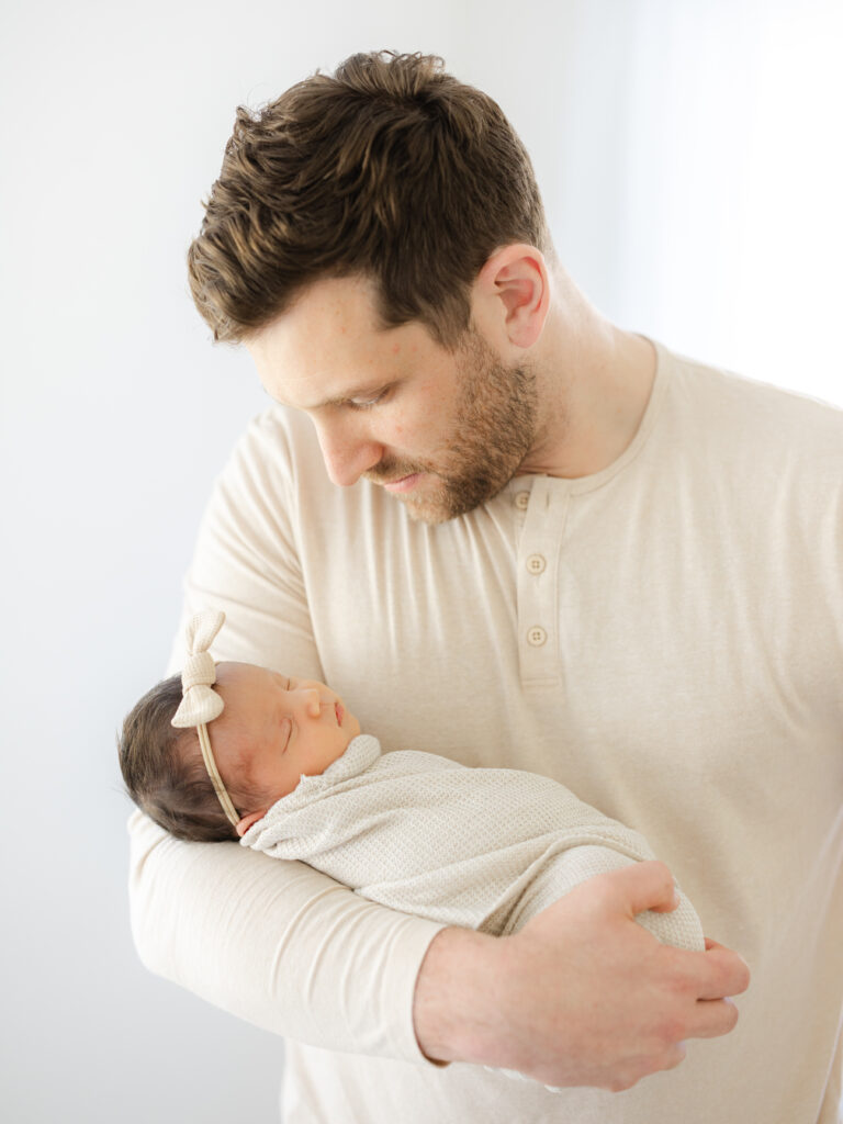 Dad holding swaddled newborn baby girl in nursery 