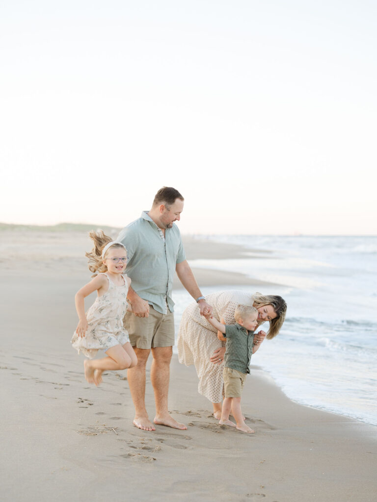 Family of four dressed in green and tan playing and holding hands on north end beach 
