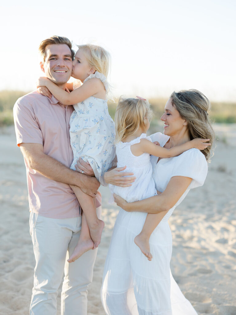 Family of four hugging on north end beach dressed in neutral pastel clothing