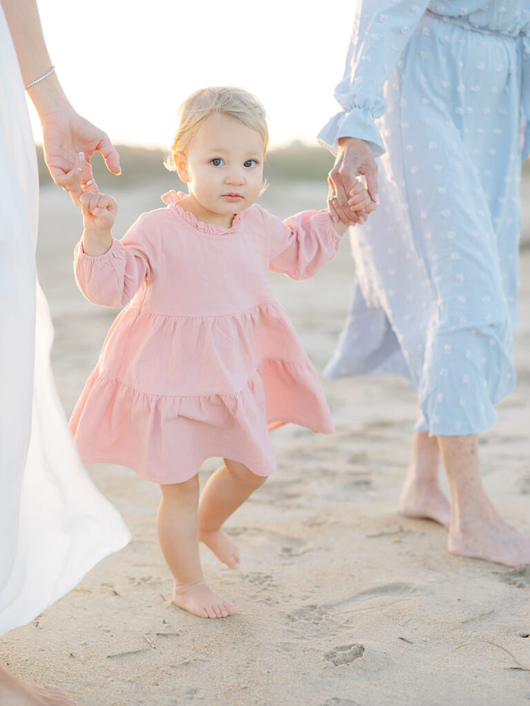 Toddler girl dressed in pink holding hands with two women walking on beach by Virginia Beach mom and family photographer Ashley Brickner 