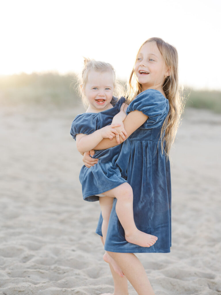 Two toddler girls dressed in matching blue dresses on beach by Virginia Beach mom and family photographer Ashley Brickner 