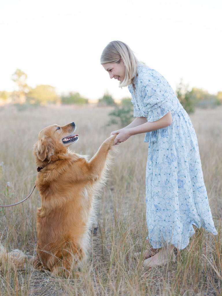 Woman in blue floral dress holding dog in field for a family photo with dog by Ashley Brickner 