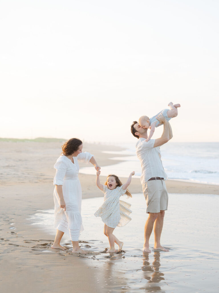 Family of four playing on beach in neutral clothes for Virginia Beach summer photos by Ashley Brickner 