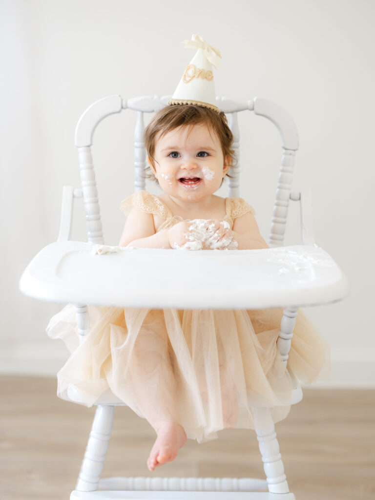 Baby girl sitting in high chair in dress in Virginia Beach photography studio 