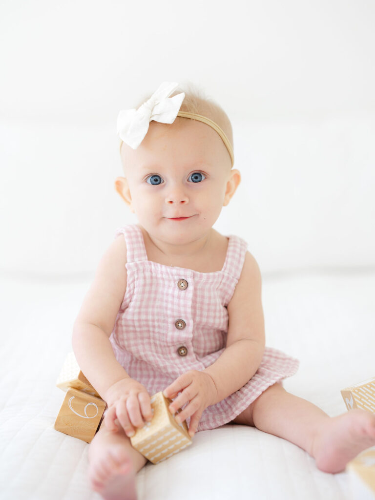 Baby girl in pink sitting up and playing with blocks during milestone session photography by Virginia Beach photographer Ashley Brickner 
