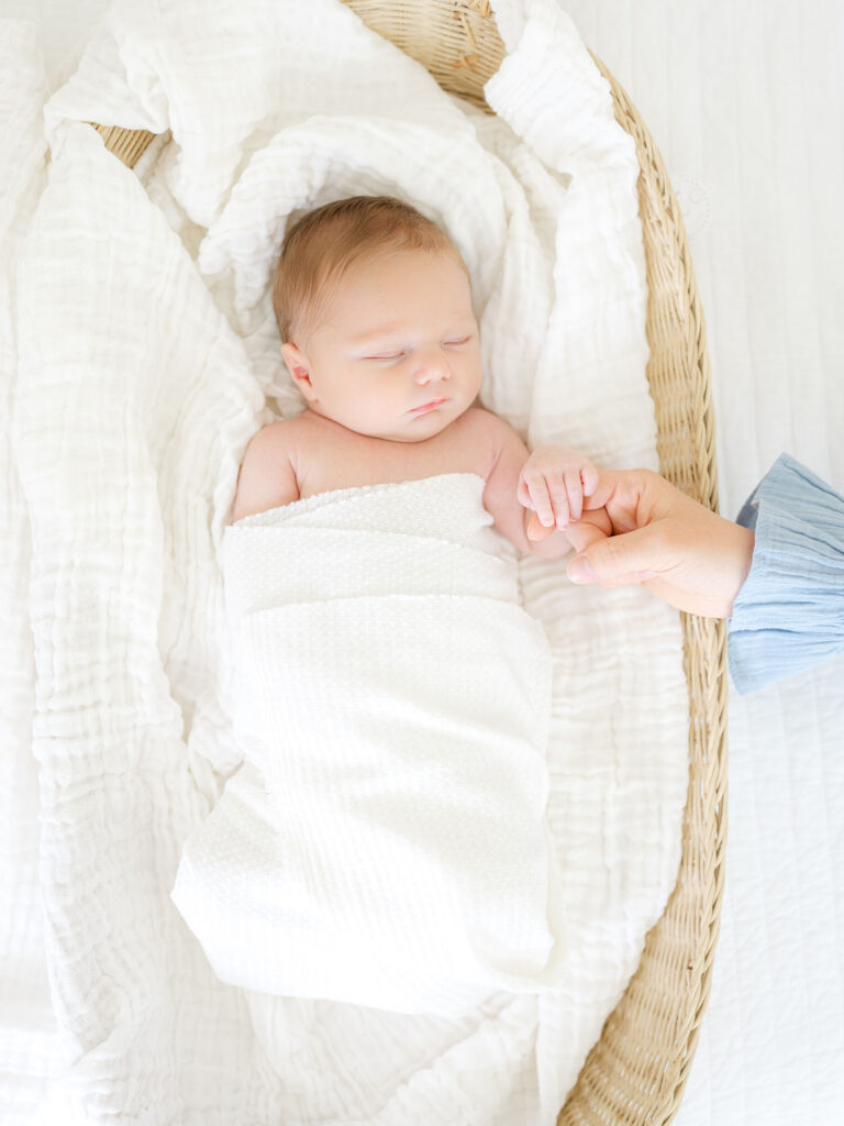 Swaddled newborn baby boy holding mom's hand during milestone session photography by Virginia beach photographer Ashley Brickner 