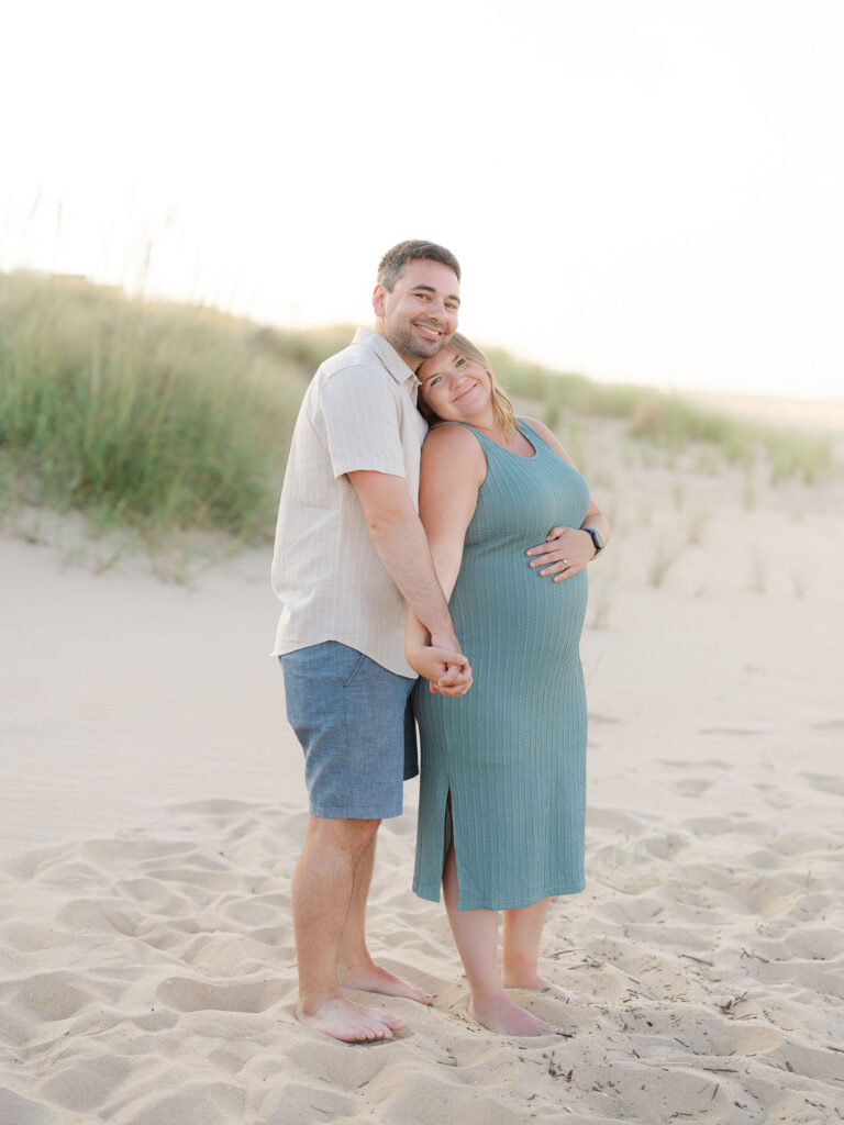 Man and pregnant woman standing on beach for summer maternity photos by Ashley Brickner 