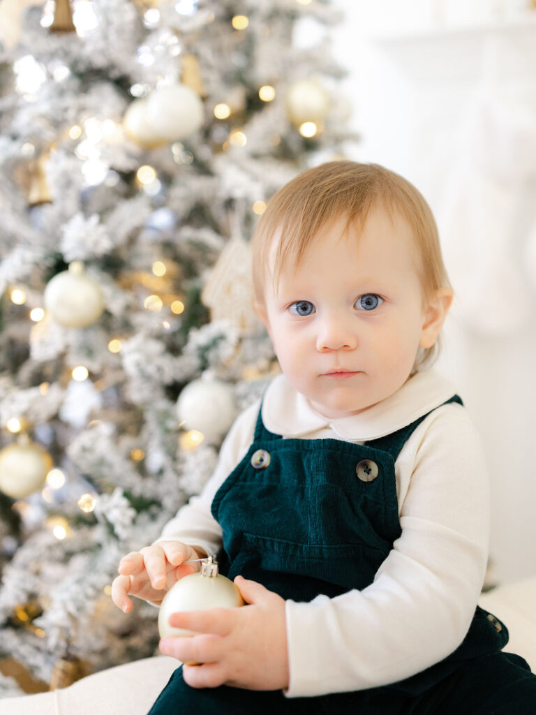 toddler boy dressed in green overalls with christmas setup 